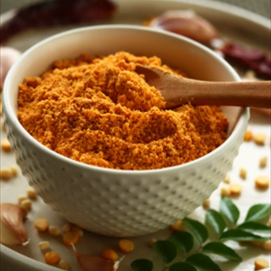 Podi in a white bowl with a wooden spoon, dried chillies and curry leaves around it