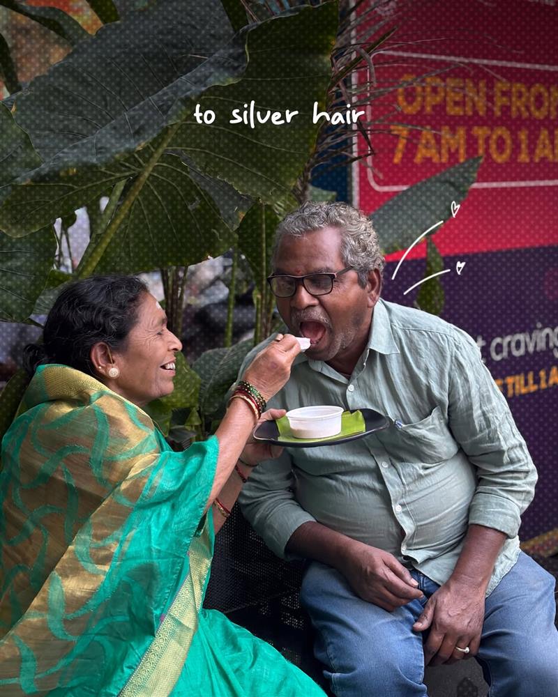 An older couple outside Babai Tiffins, one feeding the other