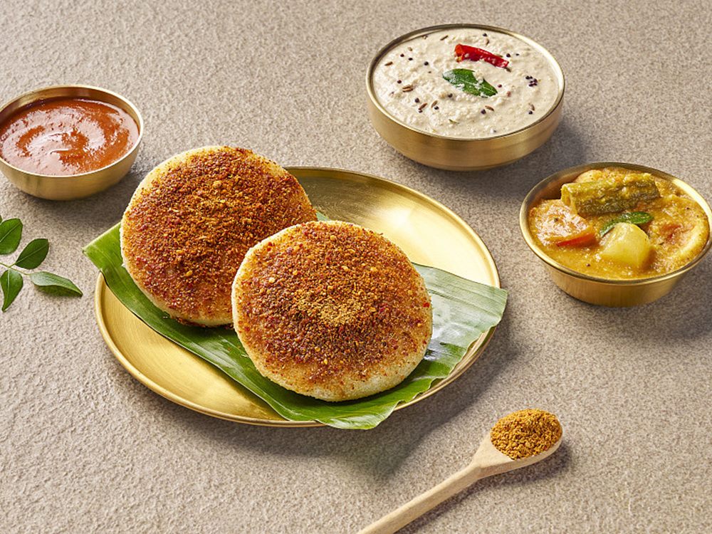 Two ghee karam idlis under a thick layer of podi, with chutneys and sambar