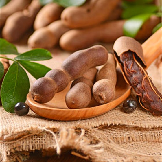Tamarind pods on a wooden spoon, one broken open to show the pulp