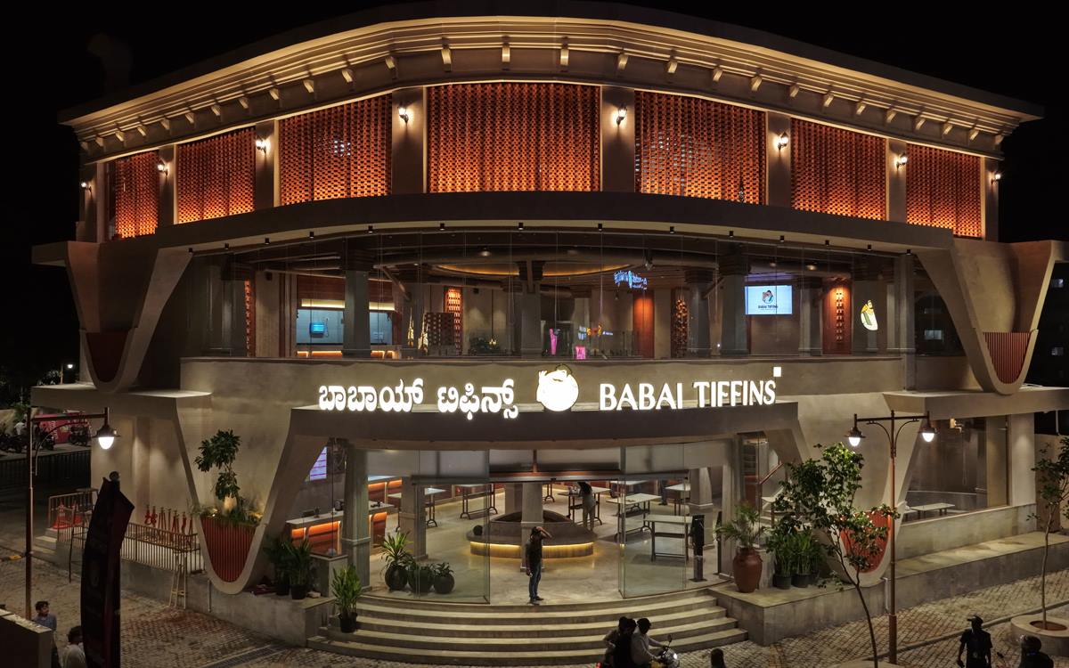 Babai Tiffins Varthur at night, the curved terracotta jaali facade lit from within