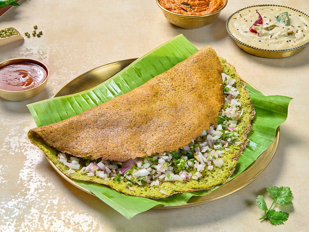 Pesarattu folded over upma on a banana leaf, chutneys behind
